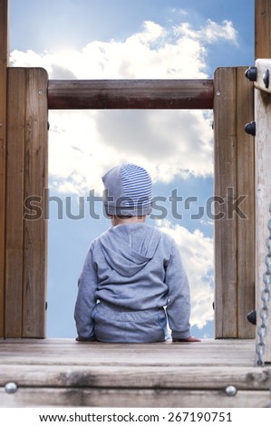 rear view of a little boy sitting and looking at the sky
