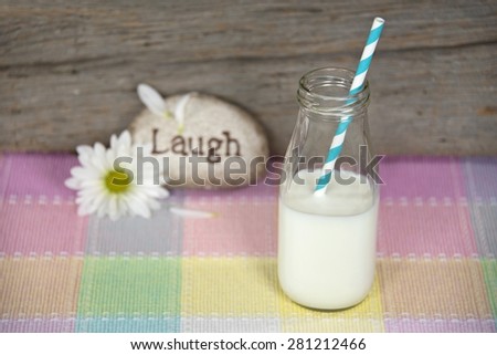 striped straw and white milk in retro milk bottle with daisy and rock on plaid fabric