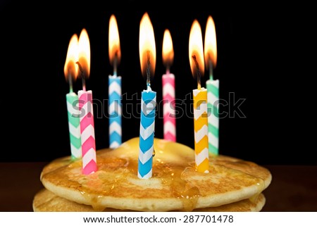 lit birthday candles on a stack of pancakes with butter and dripping syrup