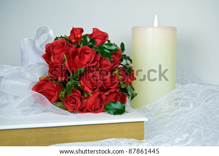 red rose and holly bridal bouquet on Holy Bible with candle and lace