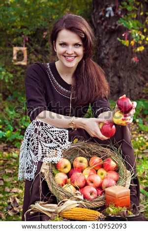 Smiling pretty young woman with apples in the hands in autumn park and a basket of apples