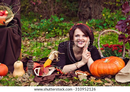 Smiling pretty young woman lying on the foliage near the vegetables in the autumn park