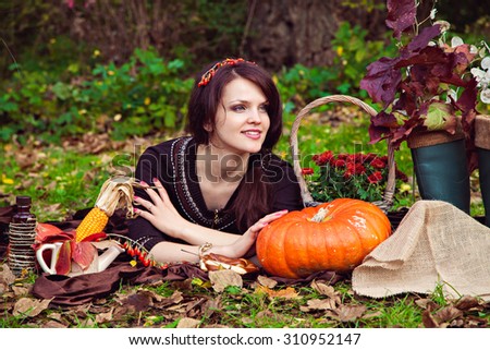 Smiling pretty young woman lying on the foliage near the vegetables in the autumn park