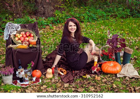 Smiling pretty young woman sitting on the foliage near the vegetables in the autumn park