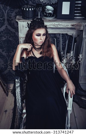 Gothic young woman in an elegant black dress in dark room