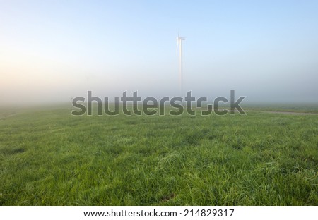 Wind turbine in a foggy meadow at dawn