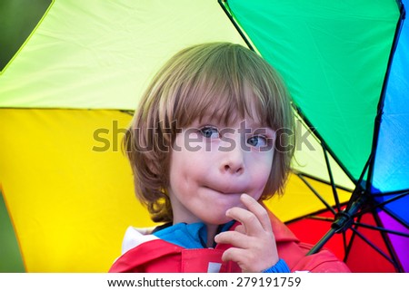 Closeup of an adorable little boy with rainbow colors umbrella in the rain