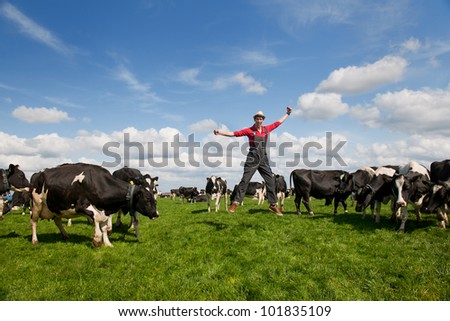 Happy young farmer jumping in field with cows