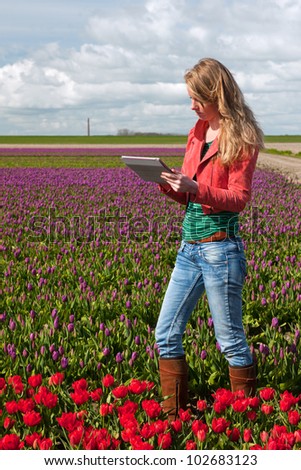 Dutch girl with long blond hair and digital tablet PC in flower fields
