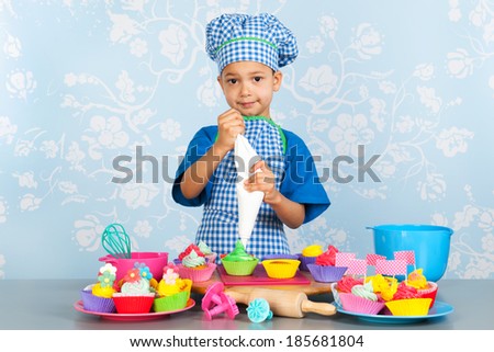 Little boy is baking colorful cupcakes with vintage wall paper in background