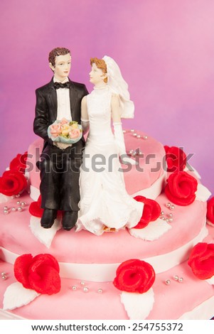 Couple on top of pink wedding cake with red roses isolated over white background