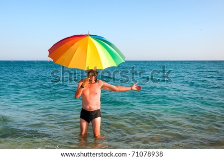 Elderly man standing in swimming trunk at the sea under the umbrella