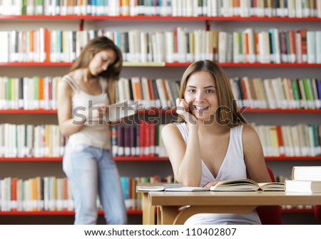 Portrait of a smiling student in a library. Young woman reading a book on background