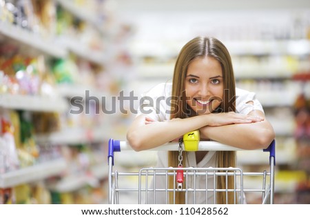 Happy blonde shopper smiles over supermarket shopping cart
