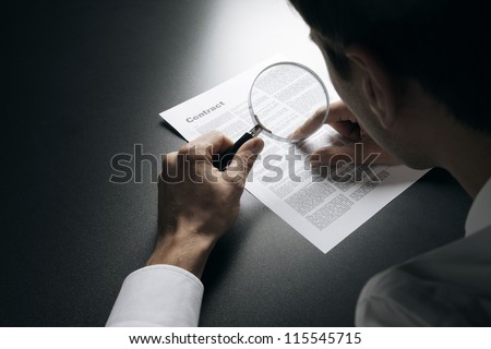 Young businessman looking to a contract through a magnifying glass