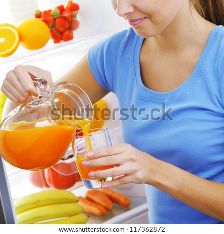 young woman near a refrigerator pouring orange juice, hands close up