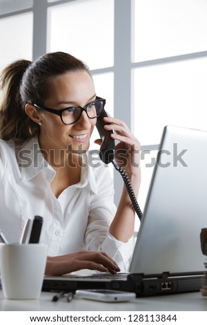Beautiful young woman working in office and making a phone call