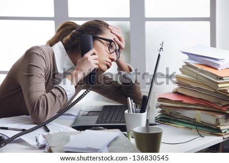 A stressed business woman looks tired  she answer telephones in her office