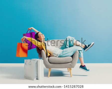 Cheerful happy shopaholic woman with lots of shopping bags, she is sitting on an armchair and celebrating with arms raised Сток-фото © 