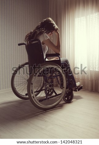 Crying woman sitting in wheelchair by window