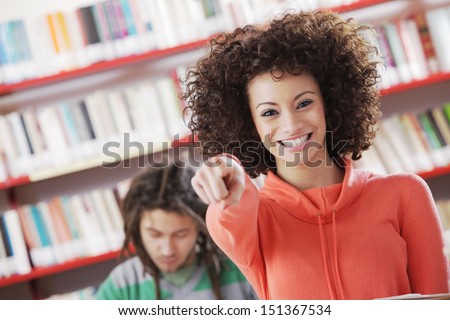 Beautiful girl pointing at you in a library