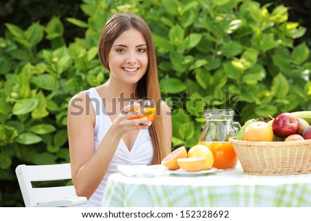Young woman relaxes in the garden drinking a orange juice