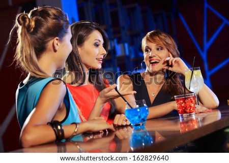 Three young women having a drink and talking in a night club