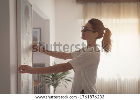 Woman hanging a painting at home and decorating her contemporary living room Stock fotó © 