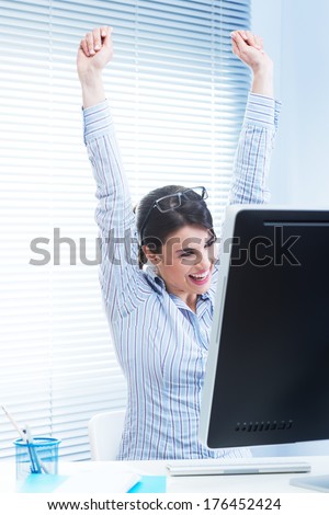 Young joyful woman at desk with fists raised receiving good news.