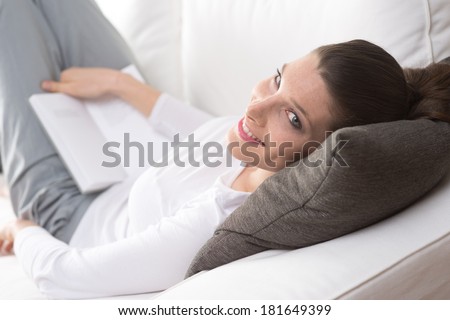 Beautiful young woman lying down on sofa and reading a book.