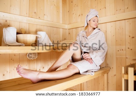 Young woman relaxing in sauna lying on a bench with eyes closed.