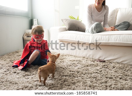 Cute superhero child and mother spending time together in the living room playing with dog.