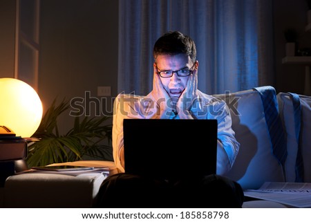 Shocked businessman with head in hands staring at laptop screen late at night.