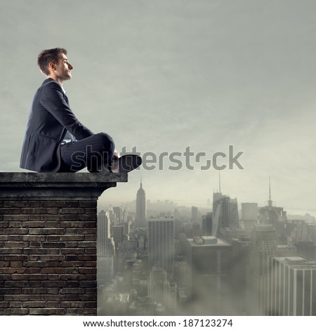 Businessman sitting on top of a building looking far away with cityscape on backgound.