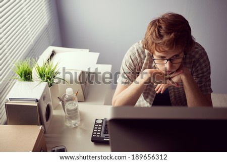 Young bored guy at office staring at computer screen.
