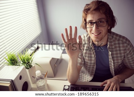 Young friendly guy smiling on web cam and waving hand.