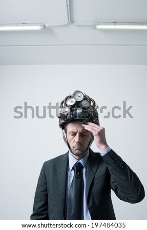 Tired pensive businessman touching his forehead weaaring futuristic helmet with gauges.