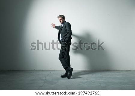 Tired pensive businessman leaning on a wall in an empty room with dramatic lighting.