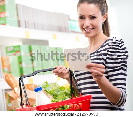 Woman at supermarket holding a full shopping basket and a shopping list.