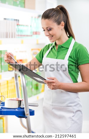 Attractive female sales clerk at work holding a clipboard with supermarket shelf on background.