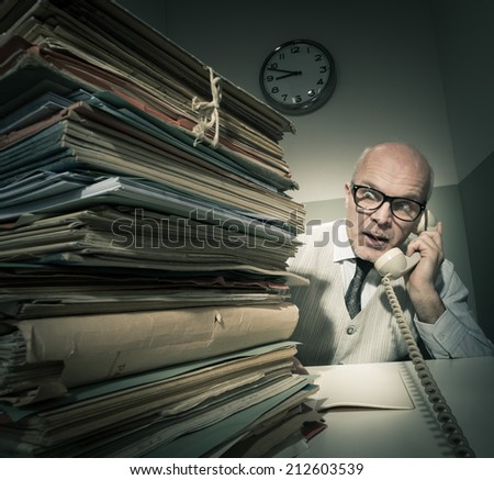 Vintage senior businessman on the phone with a huge stack of files.