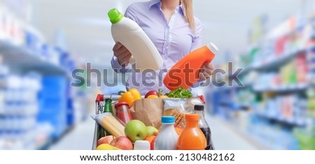 Woman doing grocery shopping at the supermarket and comparing products, she is checking two bottles of laundry detergent Foto stock © 