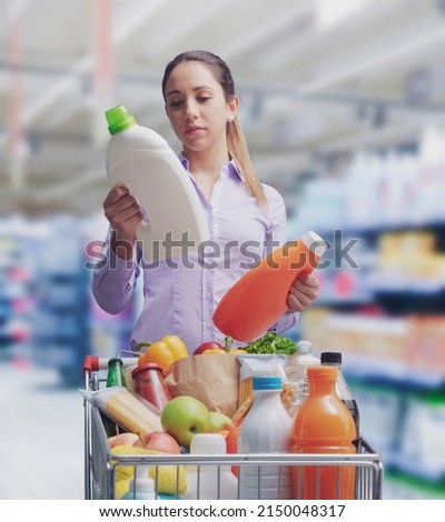 Woman doing grocery shopping at the supermarket and comparing products, she is checking two bottles of laundry detergent Stock foto © 