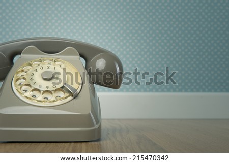 Gray vintage phone on hardwood floor and dotted light blue wallpaper on background.