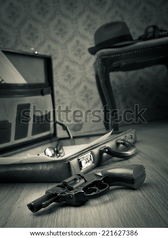 Detective open briefcase with vintage gun on the floor and borsalino hat on background.