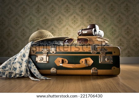 Vintage luggage with sunglasses, camera and straw hat on wooden floor.