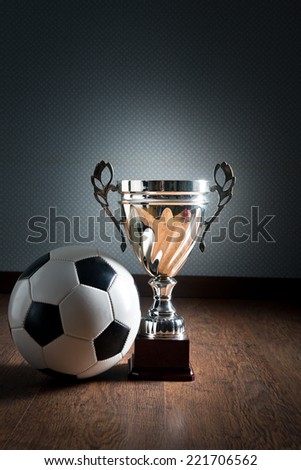 Gold cup trophy and soccer ball on hardwood floor, winning concept.