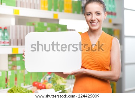 Smiling woman holding a blank sign with supermarket shelf on background.