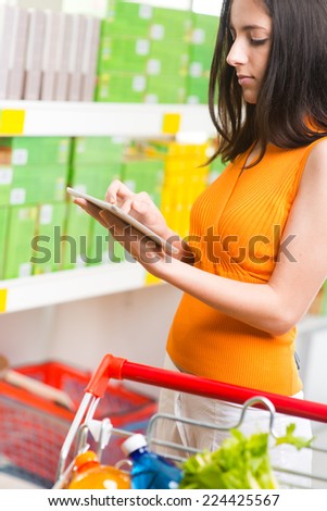 Young woman at supermarket shopping with digital tablet and shelves on background.