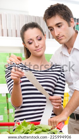 Young couple at supermarket checking a long receipt with shopping cart on foreground.